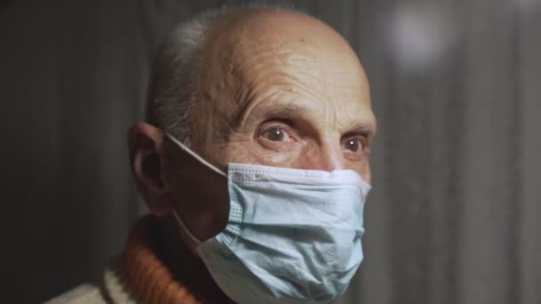 Elder man with wrinkled face in protective mask looking at camera with pain — Stock Video