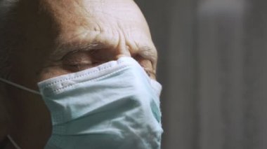Koruyucu yüz maskesi takan kıdemli bir adam karanlık hastane odasında gözlerini kapattı.