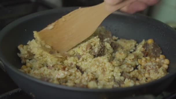 Męska ręka z drewnianą łyżką wymieszać ryż na czarnej patelni w kuchni — Wideo stockowe
