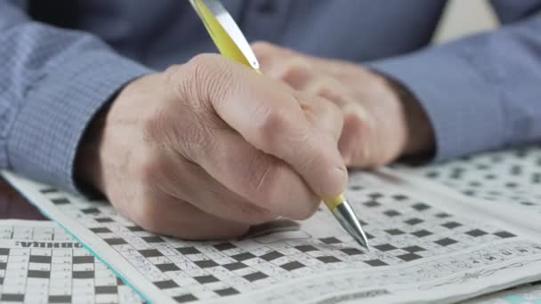 Old man with pen in wrinkled hand writing words in crossword or sudoku — Stock Video