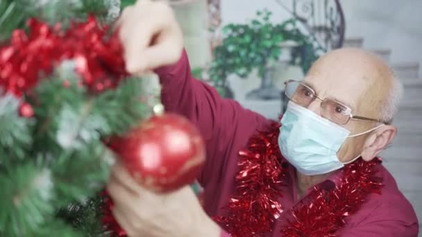 Older man wearing glasses and medical face mask decorate Christmas tree — Stock Video