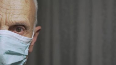 Tıbbi maske takan kıdemli bir adamın yüzünün yarısı hastane odasında yakından görülüyor.