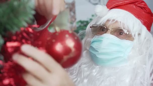 面白いサンタクロースでfacemask赤ボールとクリスマスツリーを飾る — ストック動画