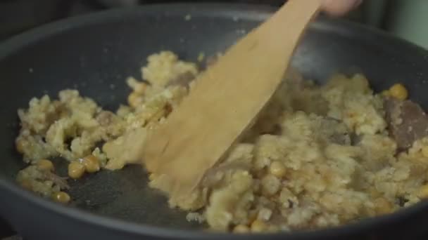 老厨师用木桨把饭和肉混合在黑锅里 — 图库视频影像