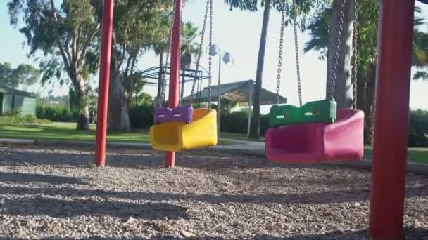 Bunte Kinder schaukeln im Wind auf leerem Spielplatz in Quarantäne. — Stockvideo