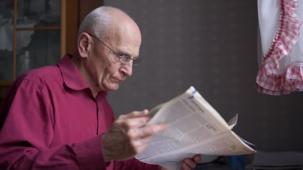 Homem mais velho Hoary usa óculos lê jornal com cuidado — Vídeo de Stock