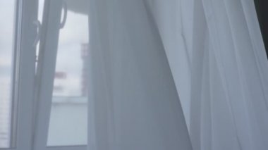 Şiddetli rüzgar pencereden eser ve odada asılı beyaz ince perde