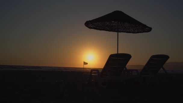 Tomt vardagsrum och parasoll på tom sandstrand vid kusten vid solnedgången — Stockvideo