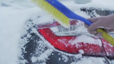 Örgü eldivenli kadın eli siyah arabanın arka ışığından kar temizliyor.