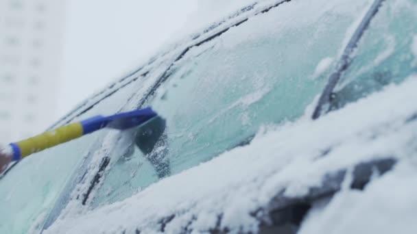 Жінка рука тримає різнокольоровий щітковий скраб і очищає сторону крижаного скла автомобіля — стокове відео
