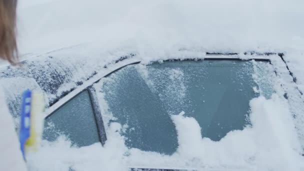 Женская рука с кистью в руке выметает снег из бокового окна черного автомобиля — стоковое видео