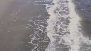 Beyaz köpüklü çamurlu deniz suyu kumlu deniz kıyısında akıyor.