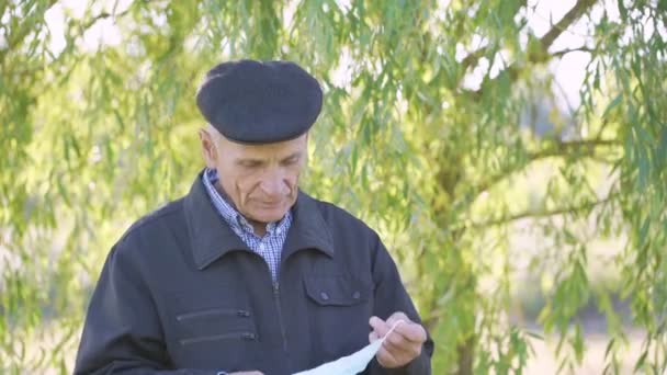 Anciano hombre usando gorra tratando de poner en médico protector mascarilla — Vídeos de Stock