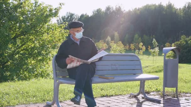 Homme âgé portant un masque médical et lunettes de lecture journal extérieur. — Video