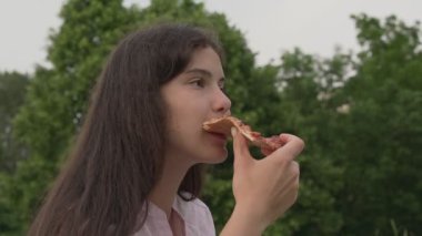 Şehir parkında pizza yiyen genç bir kız..