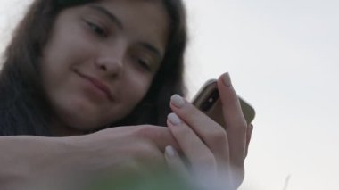 Uzun kahverengi saçlı genç kız modern akıllı telefondan mesaj yazıyor..