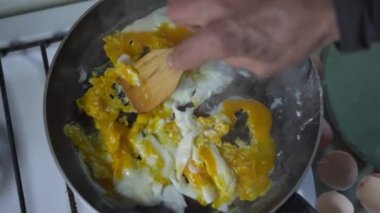 Tahta spatulası olan, tavada yumurta karıştıran ve kahvaltı hazırlayan bir adam..