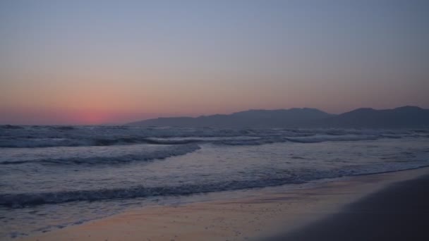 夕阳西下，海浪在空旷的沙滩上流过，映衬着高山的轮廓. — 图库视频影像