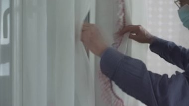 Gözlüklü ve koruyucu maskeli büyükbaba perdeyi açtı ve elini salladı.