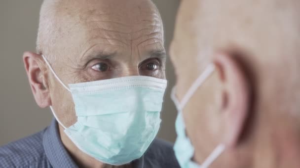 Äldre man bär medicinsk mask ser sig i spegeln med sorgsna ögon — Stockvideo