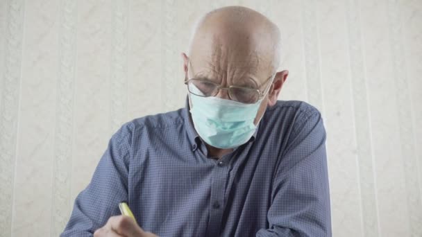 Viejo canoso con gafas se sienta a la mesa y escribe carta con bolígrafo — Vídeo de stock
