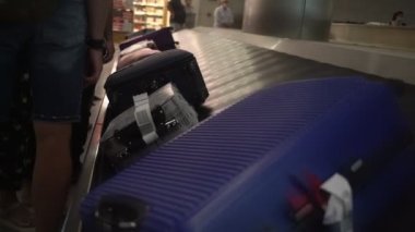 Havaalanı binasında bavullu insanlar konveyör bandında kuyruğa giriyor.