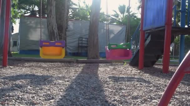 Bambini altalene di plastica che si muovono su un parco giochi vuoto sotto la luce del sole. — Video Stock