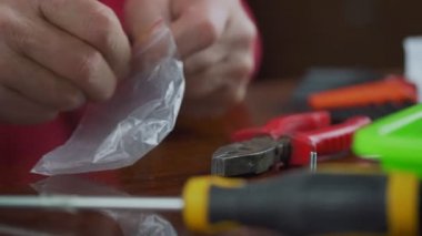 Older man with aged hands takes metak screws and put into plastic packing box.