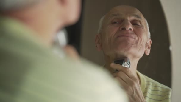 Cheerful active elderly man looking at mirror and shaving his chin. — Wideo stockowe