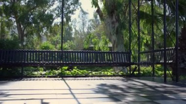 Empty summer house with long bench and tropical plants and trees around.
