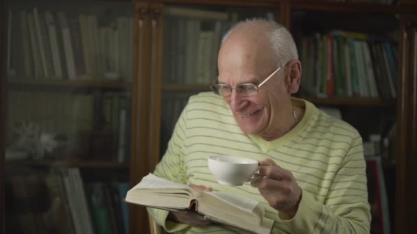 Glücklich fröhlicher Mann mit Brille liest Buch und hält Tasse Kaffee in der Hand. — Stockvideo