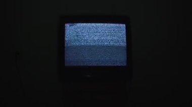 Gece siyah odada gürültülü analog statik sinyalli kırık bir televizyon ekranı.