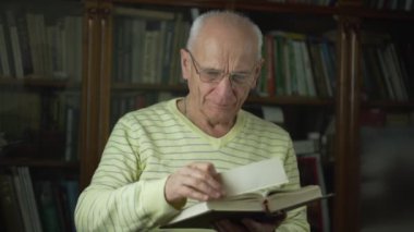 Gözlük takan yaşlı adam elinde kitap ayracıyla İncil okuyor..