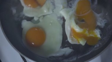 Elinde tahta sopa olan bir adam siyah tavada kızarmış yumurta karıştırıyor.