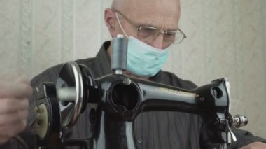 Yüz maskeli otantik bir terzi ve dönen gözlüklü dikiş makinesi tekerleği..