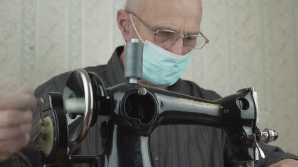 Authentieke kleermaker in gezichtsmasker en bril draaiende naaimachine wiel. — Stockvideo