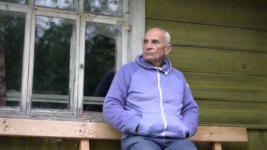Mutsuz, düşünceli, kır saçlı yaşlı adam ahşap bankta oturuyor.