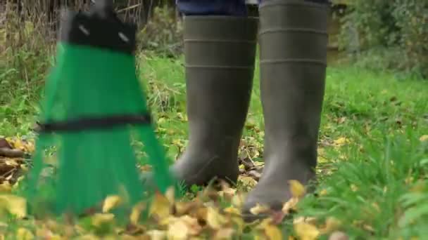 Hausmeister in Gummistiefeln fegt mit grünem Besen gelbes Laub. — Stockvideo