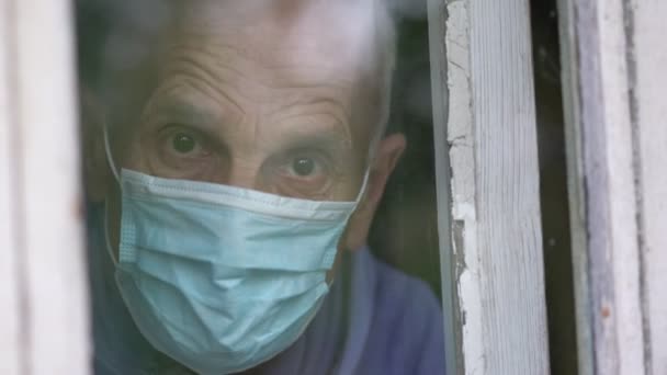 Большой видеопортрет пожилого человека в защитной маске за окном — стоковое видео