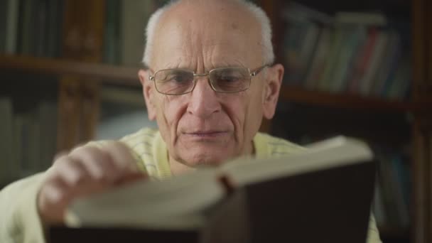 Senior man in bril blad door oude boekpagina 's close-up — Stockvideo