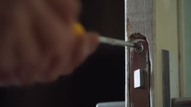 Erkek eli tornavidayı tutuyor ve metal vidayı kapı kilidine çeviriyor..