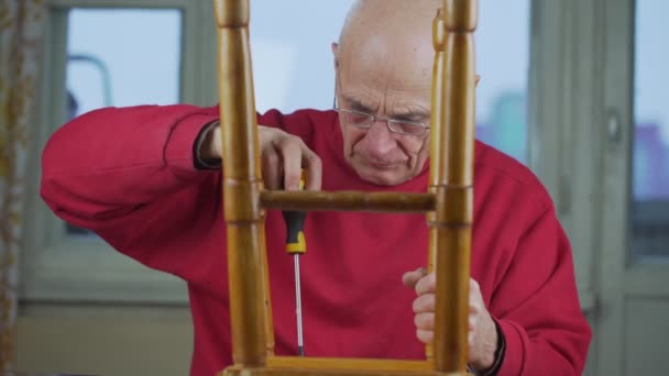 Äldre man i glasögon och med skruvmejsel i händerna reparerar träpall — Stockvideo