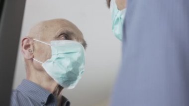 Yaşlı, savunmasız, yüz maskesi takan adam aşıdan önce aynaya bakar.