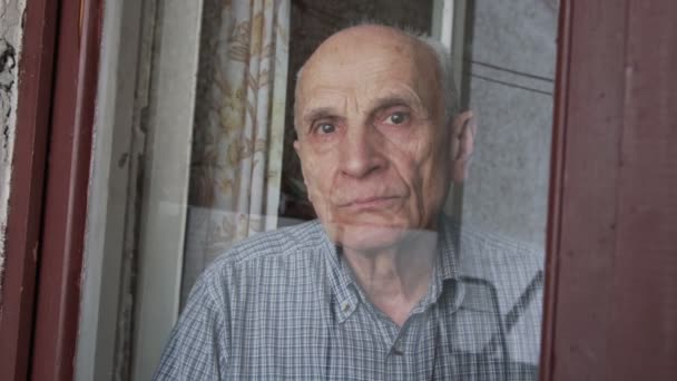 Sullen uomo anziano con gli occhi tristi guarda attraverso vetro della finestra — Video Stock