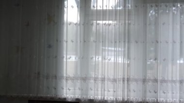 Odasında şeffaf kumaş beyaz perde asılı büyük bir pencere.
