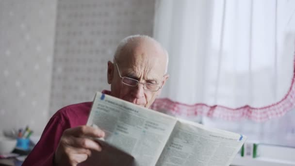 Senior mit Brille liest Zeitung und blickt in Kamera. — Stockvideo