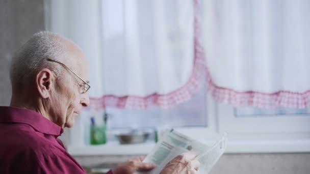 Aîné personne aux cheveux gris en feuille de lunettes à travers les pages de journaux — Video