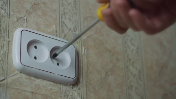 Man with screwdriver in hands turns of screw from white plastic socket on wall. — Stock Video