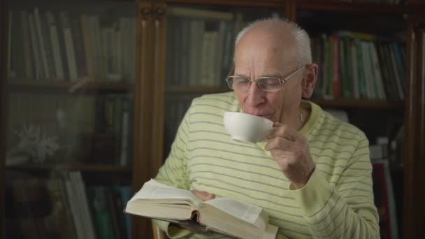 Homem feliz engraçado velho com xícara de chá ou café livro de leitura — Vídeo de Stock