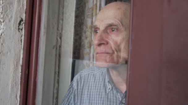 Szomorú öregember áll az ajtó mögött üveg és néz be az ablakon. — Stock videók